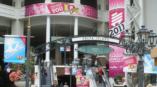 Large pink banner hanging from pillar near elevators outside a convention center.